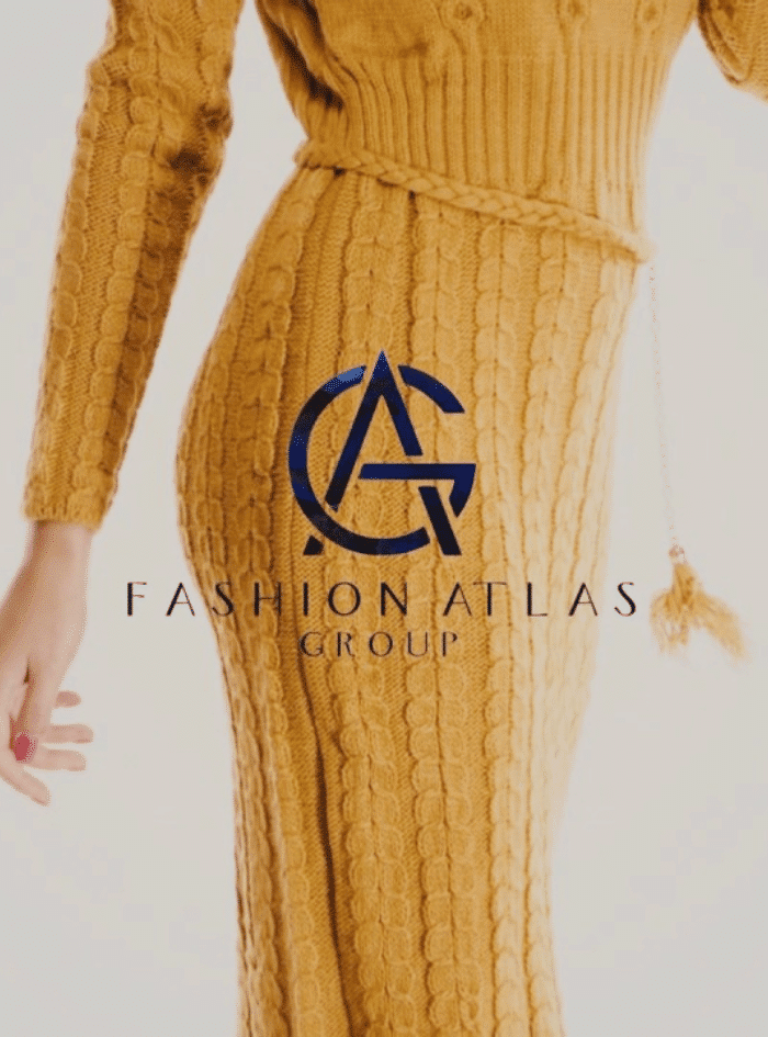 Woman in a mustard yellow cable-knit sweater dress with a matching belt poses with her left arm raised. The text overlay reads "Fashion Atlas Group" in blue with a stylized logo incorporating the letters "F" and "A".