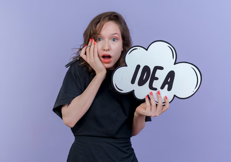 A surprised woman in a black shirt holds a marker and a cloud-shaped sign with "IDEA" written on it, standing in front of a purple background—perfect for brainstorming captivating boutique name ideas.